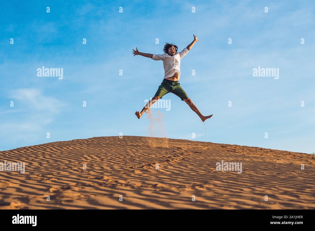 Beautiful young man jumping barefoot on sand in desert enjoying nature