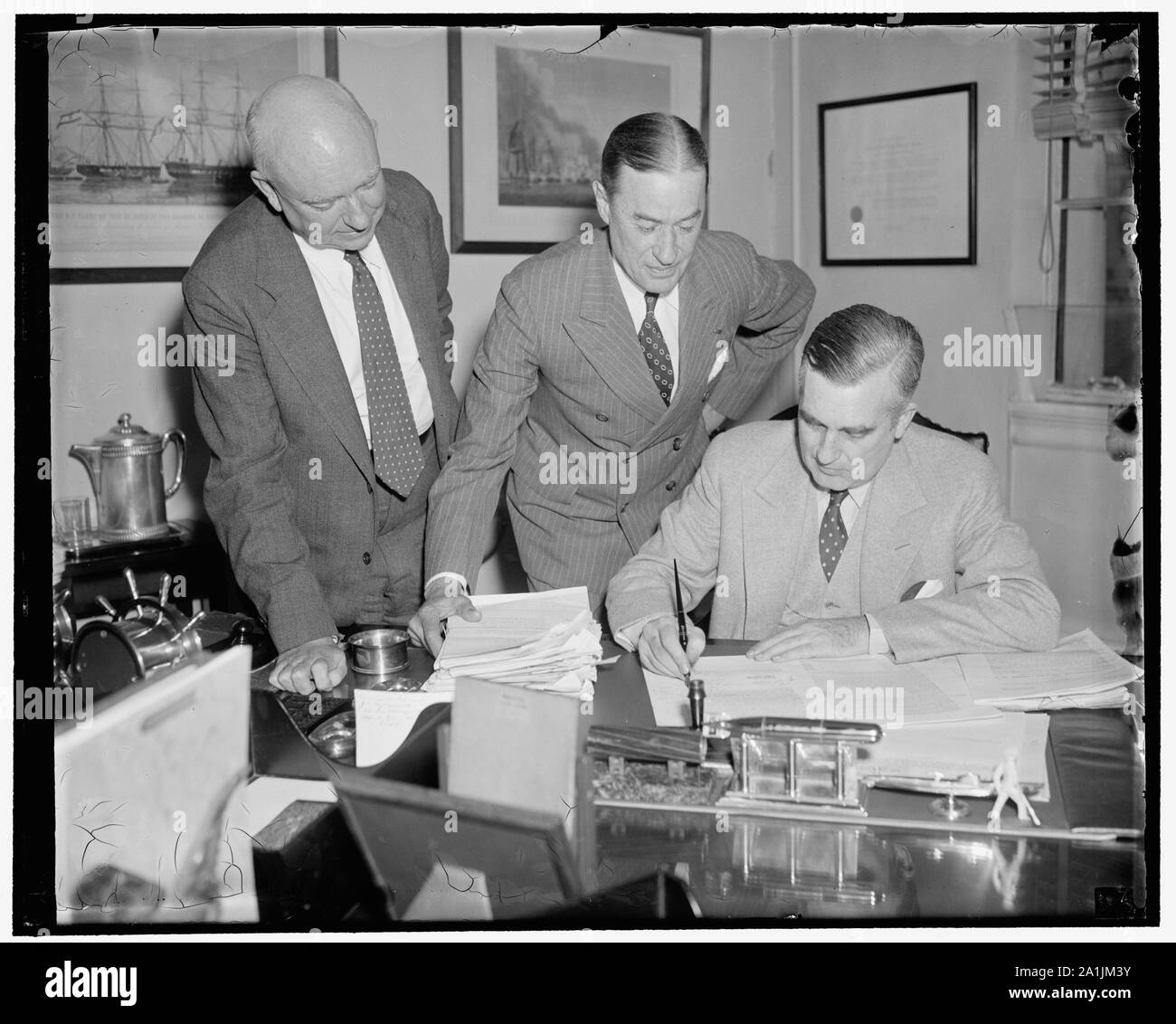 Naval increase on the way. Washington, D.C., June 2. Assist. Secretary of the Navy, Charles Edison, today signed final confirmation on awards to private shipyards for the construction of twenty-four naval vessels totaling 159,800 tons. Approximate cost will be $350,000,000. Picture shows, left to right: Warren McLaine, Assist. to Judge Advocate General of the Navy; Rear Admiral W.B. Woodson, Judge Advocate General of the Navy; and Charles Edison, Assist. Secretary of the Navy Stock Photo