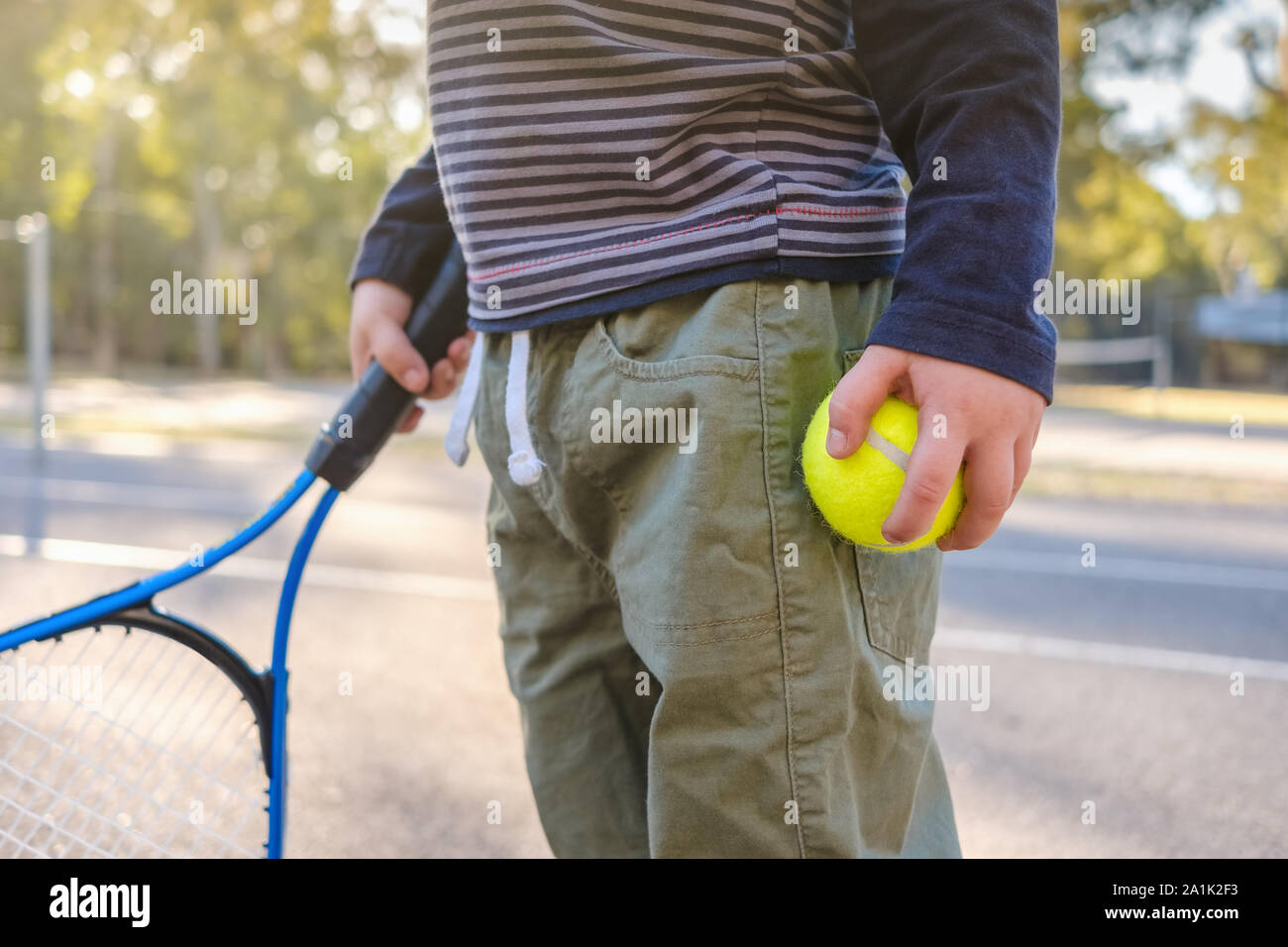 Little Australian boy holding tennis racket and ball at outdoor court in Australia Stock Photo