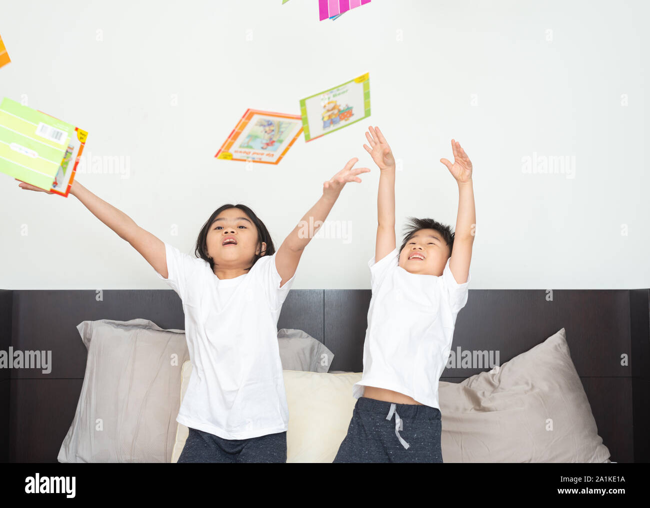 Boys and girls in pajamas throwing story books to play on the bed. Happy expression in the