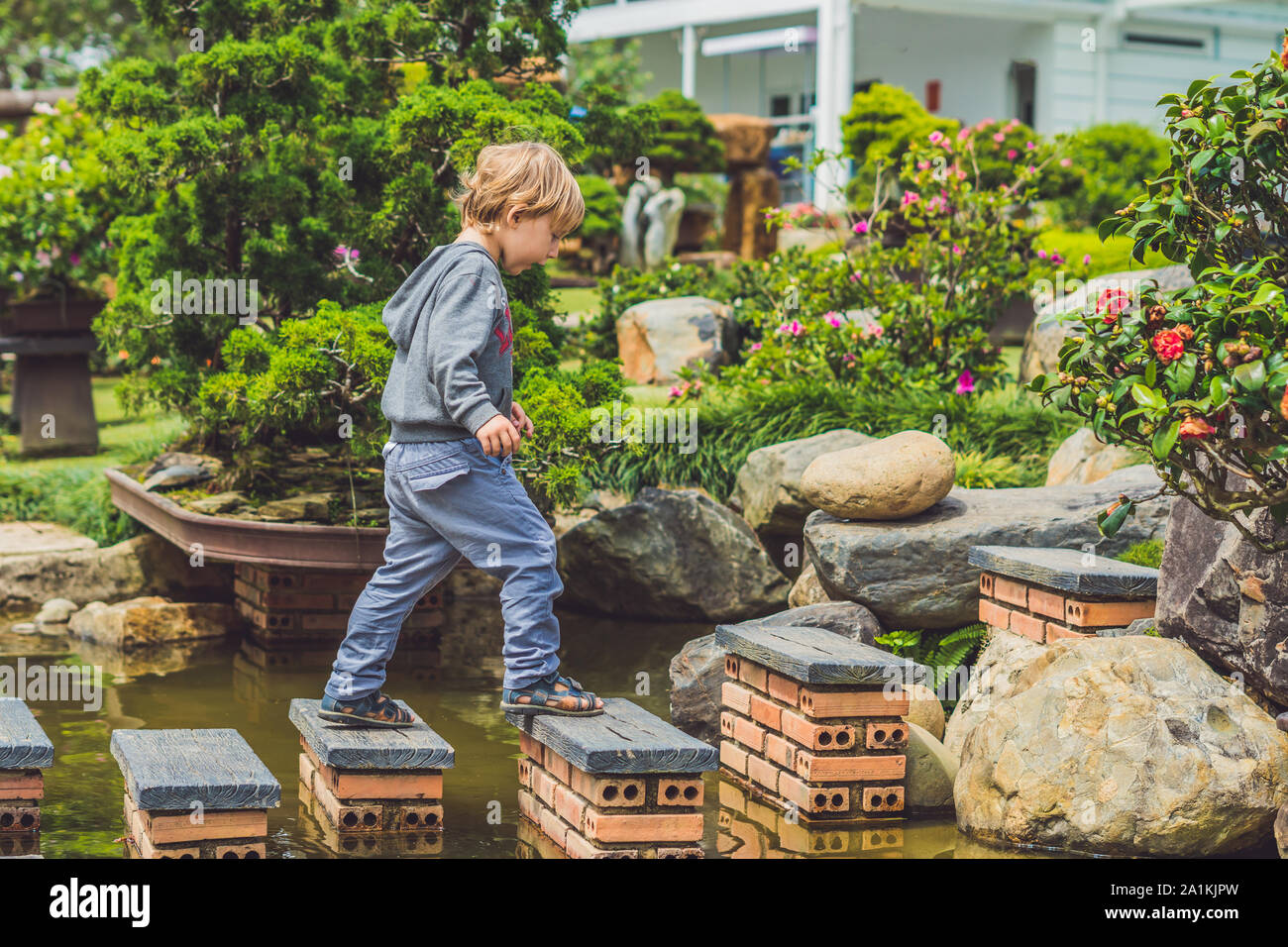 Adorable young boy with crossing river or water jumping from rock to rock. Crossing the gap, freedom, liberation, success, avoiding danger, courage Stock Photo