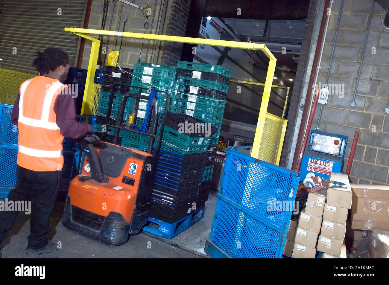 A warehouse worker moving plastic delivery crates using an electric hand truck. Stock Photo
