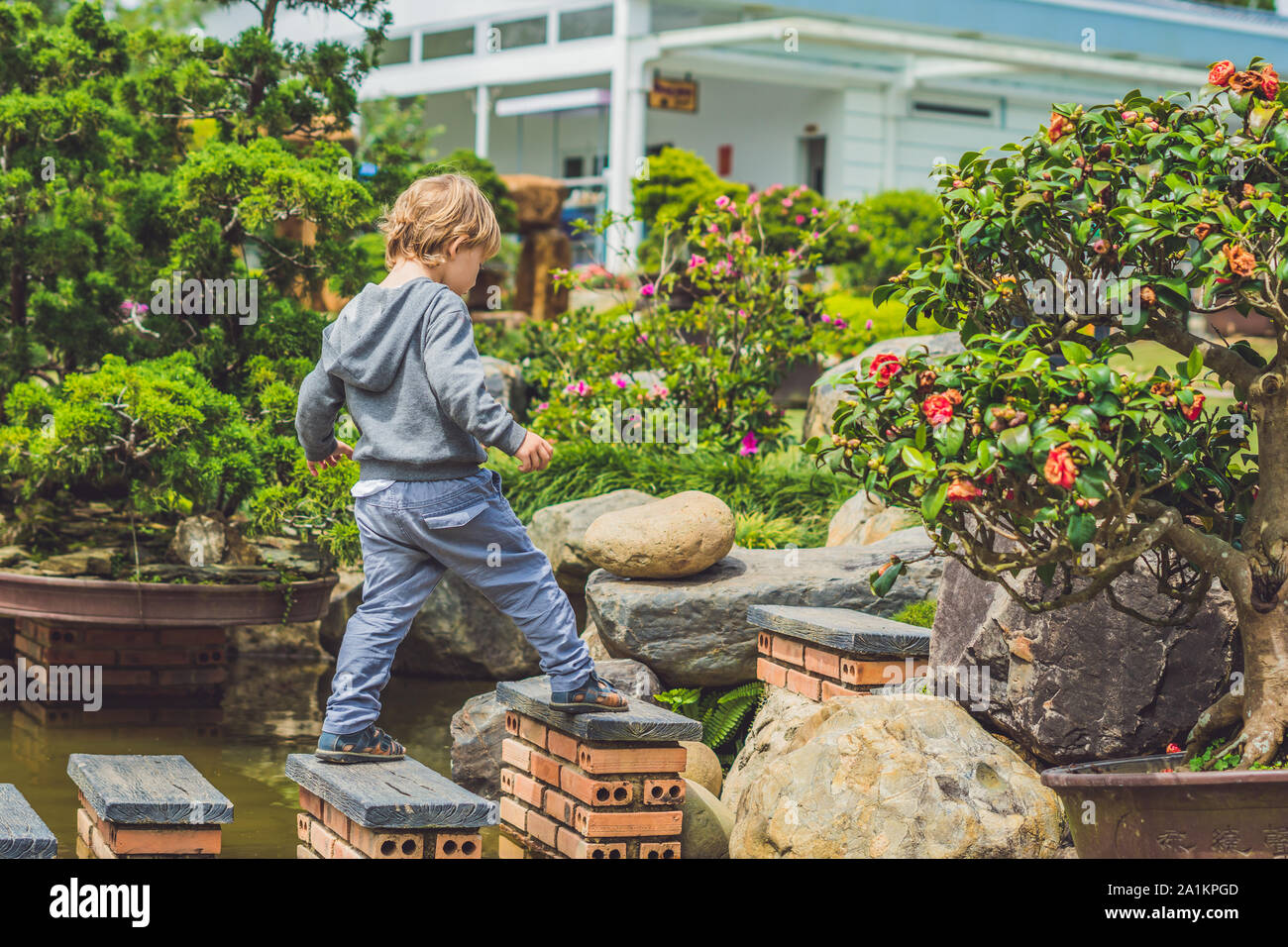 Adorable young boy with crossing river or water jumping from rock to rock. Crossing the gap, freedom, liberation, success, avoiding danger, courage Stock Photo