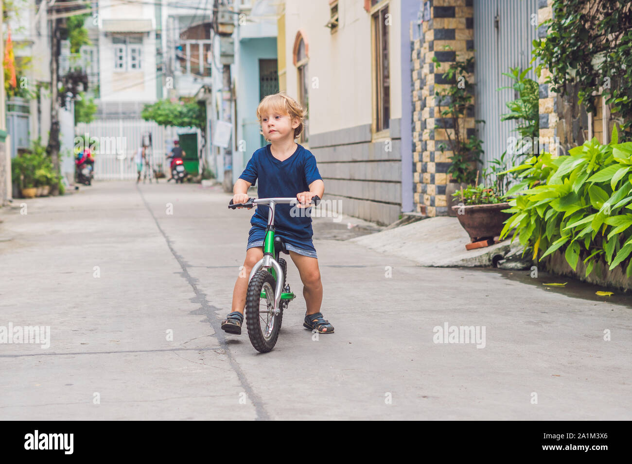 Active blond kid boy driving bicycle n the street of the city. Toddler child dreaming and having fun on warm summer day. outdoors games for children Stock Photo