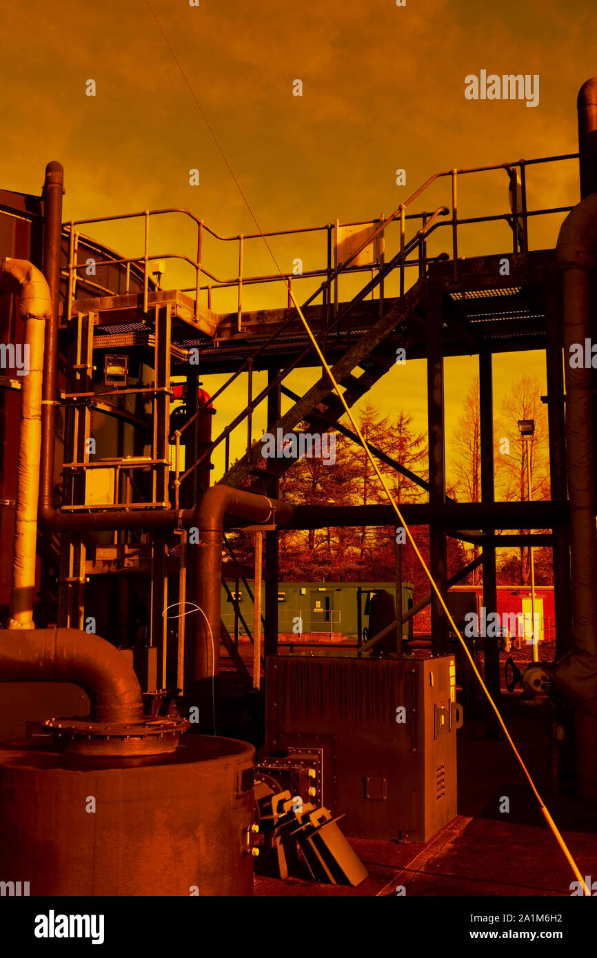 Industrial plant and equipment with ladders and pipework against sky, with gold tone. Stock Photo
