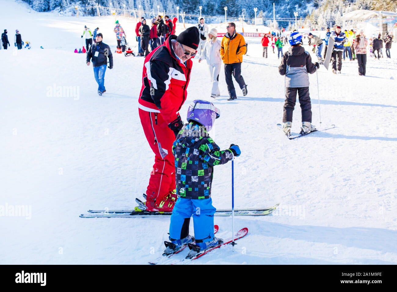 Bansko, Bulgaria - December, 12, 2015: The small child learning to ski and man on the slope in Bansko, Bulgaria Stock Photo