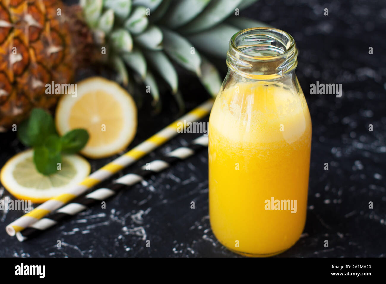 Little bottle of homemade pineapple lemonade with two straws on black background Stock Photo