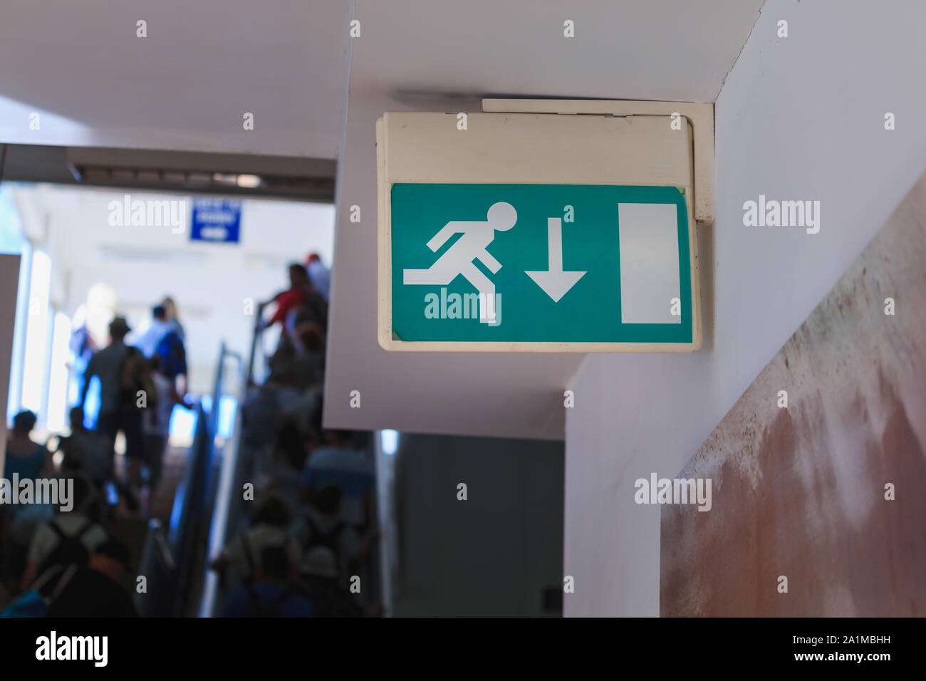 Emergency exit sign in corridor mounted on a wall. People walking in corridor background Stock Photo