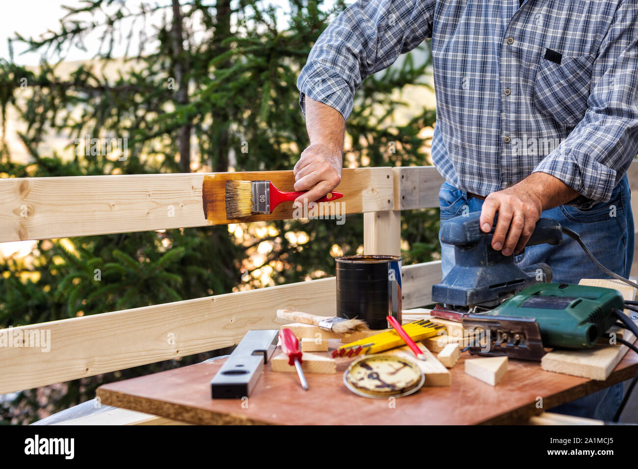 Adult craftsman carpenter with the brush painting the boards of a