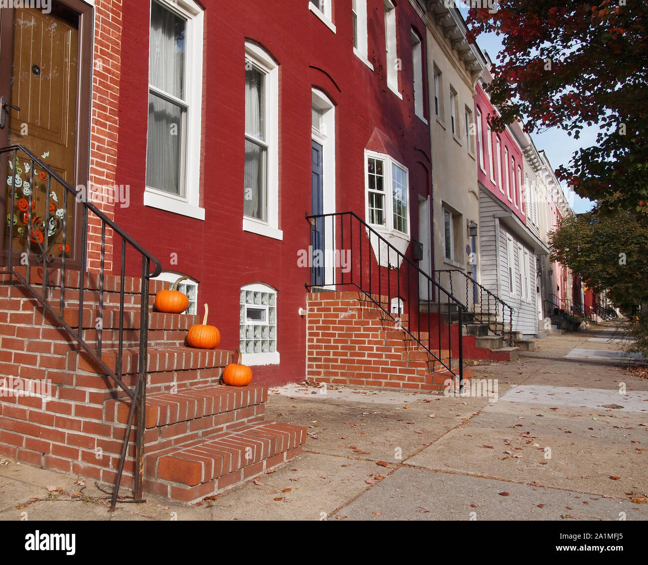 Three perfect orange pumpkins decorate the steps of a brick stoop style doorstep in an urban rowhouse neighborhood in the autumn season. Stock Photo