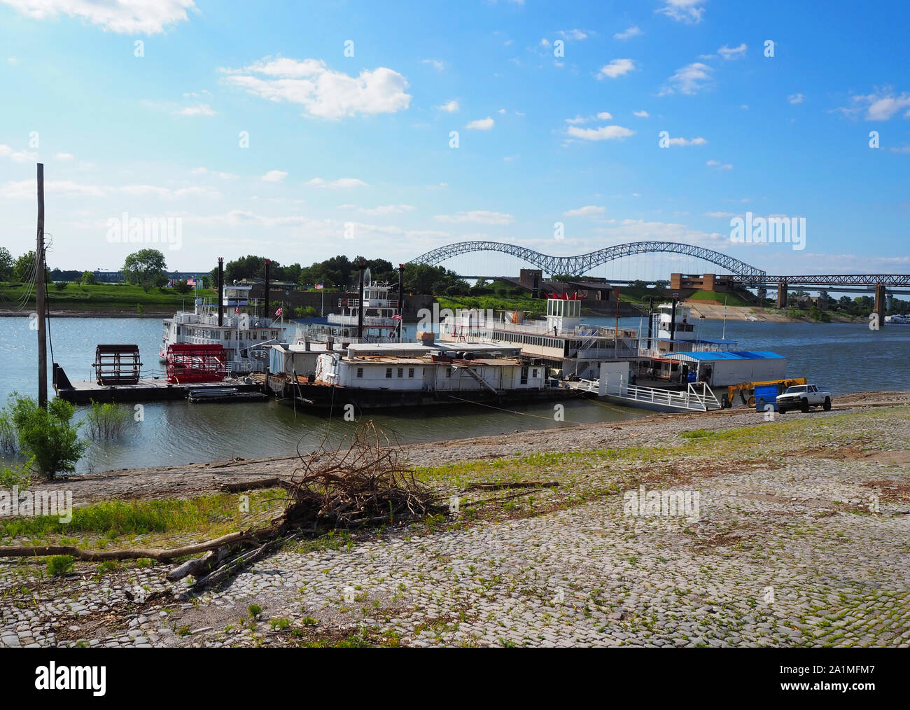 Old riversboats and and some removed paddlewheels next to the shore of the Mississippi river with the Hernando de Soto Bridge in Memphis, TN n the bac Stock Photo