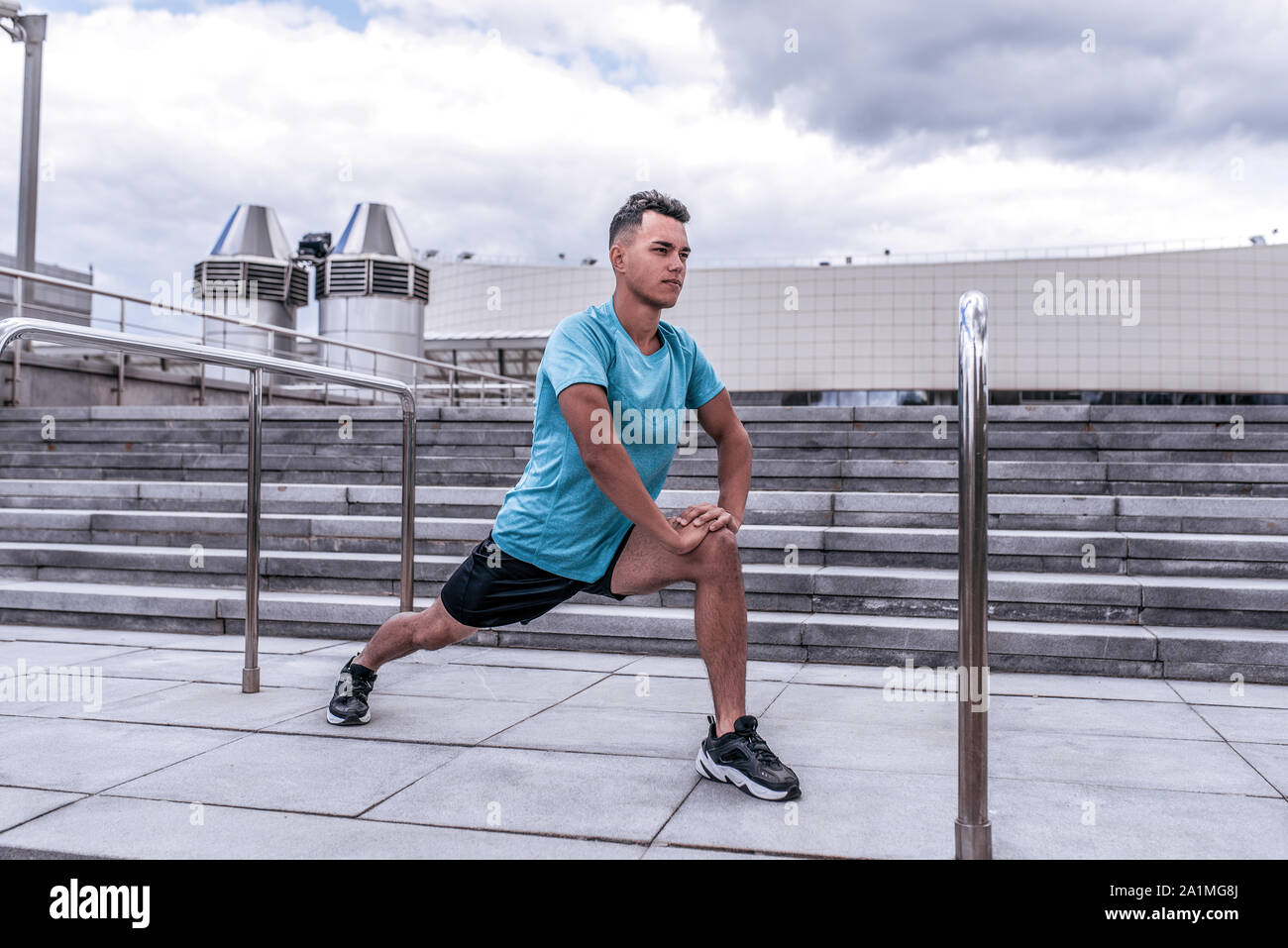Male athlete guy, in summer in city, doing warmups of knees of joints