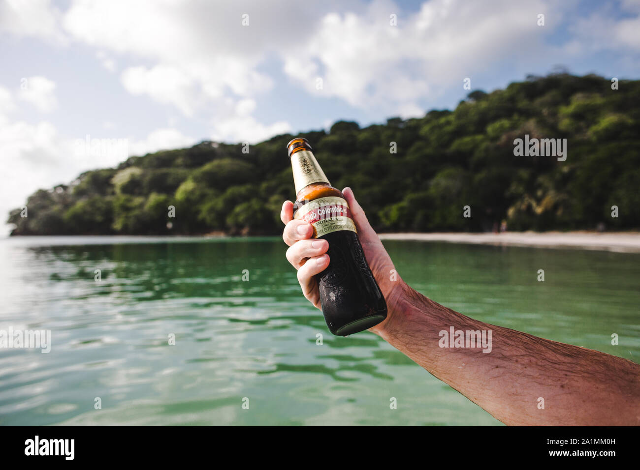 Caucasian male hand holding up a refreshingly cold bottle of Club Colombia - the premium national beer of Colombia - at a beach on a Caribbean island Stock Photo