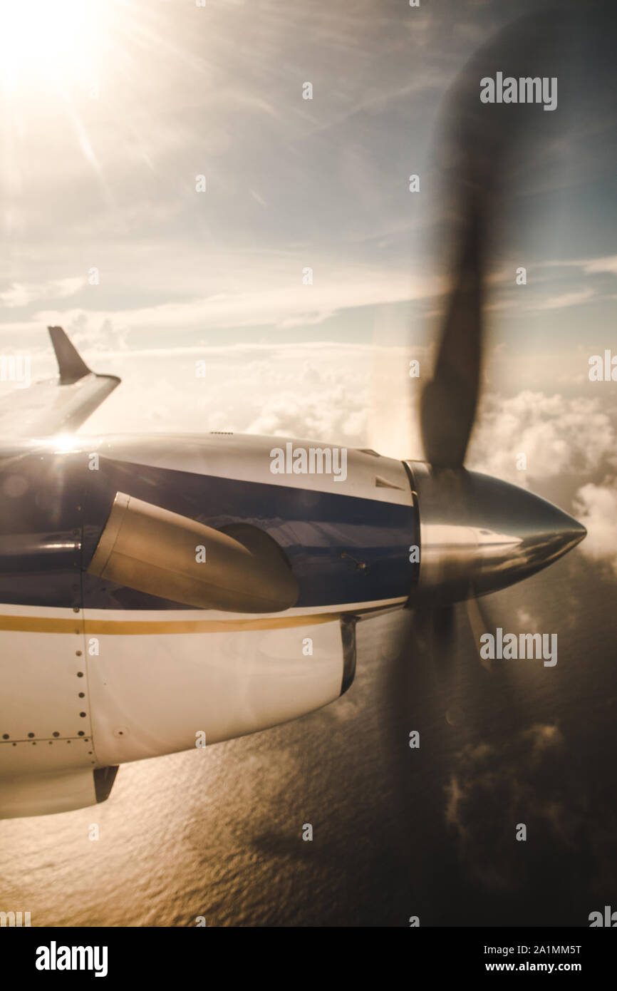 Small propeller plane flying over clouds to an island in the Caribbean Sea Stock Photo