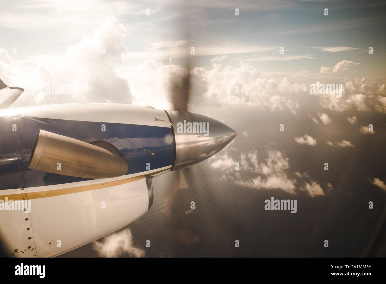 Small propeller plane flying over clouds to an island in the Caribbean Sea Stock Photo