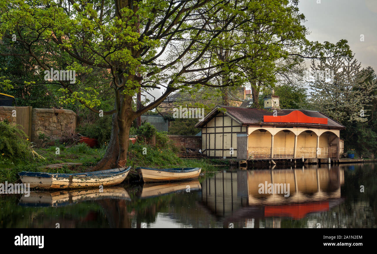The old Ashley Terrace's Boathouse and two rowing boats on a calm spring day, with reflections in the water and green grass and trees. Edinburgh. Scot Stock Photo