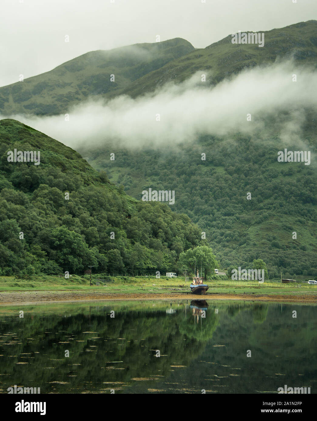 Vertical landscape. Loch Duich, near Kintail, in the Highlands of Scotland, with fishing boat on the shore, low clouds hanging around the mountains Stock Photo