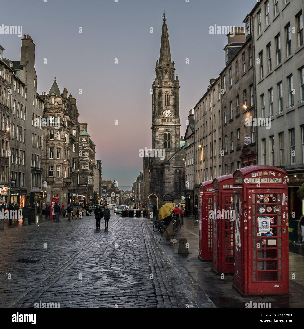 High Street in the Old Town's Royal Mile at Blue Hour. Pink and blue sky, people walking in wet cobblestone street. Red phone boxes in forground Stock Photo