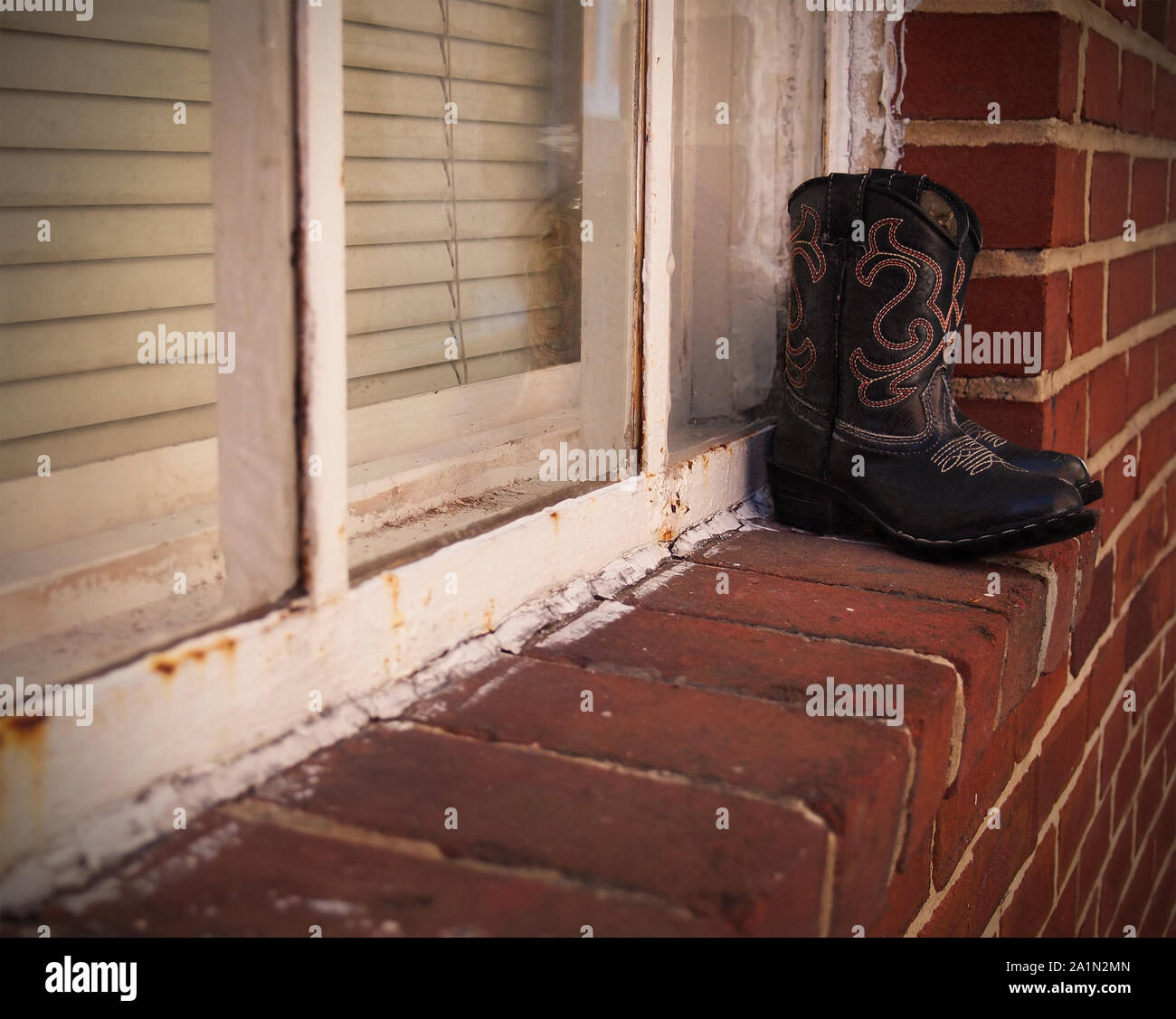A pair of black western boots with embroidery stitching rests on a brick ledge outside a home. Stock Photo
