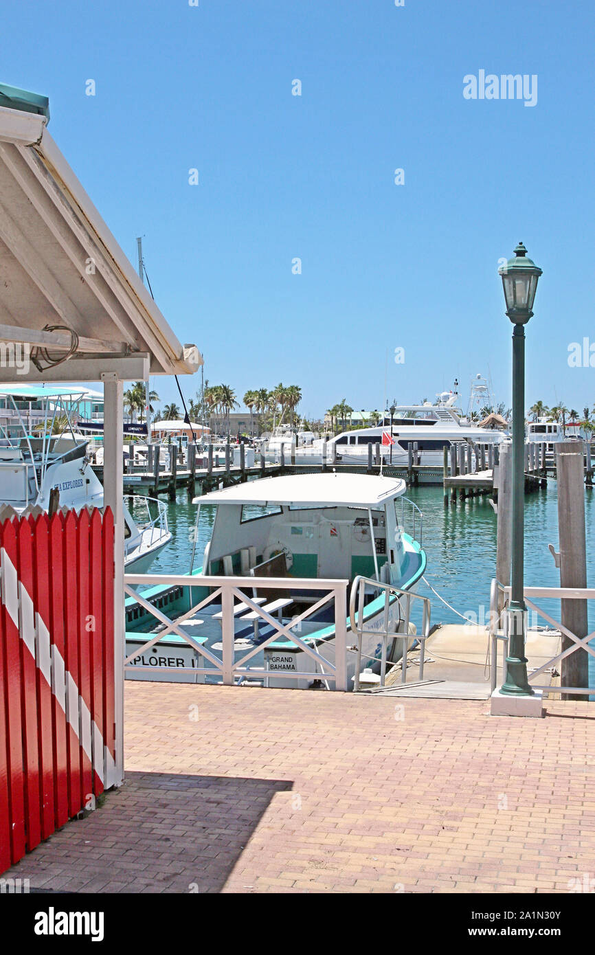 A dive flag (red with a white diagonal stripe) painted on a wooden fence gate leads the viewer's gaze onto the marina at Lucaya, Grand Bahama Island. Stock Photo