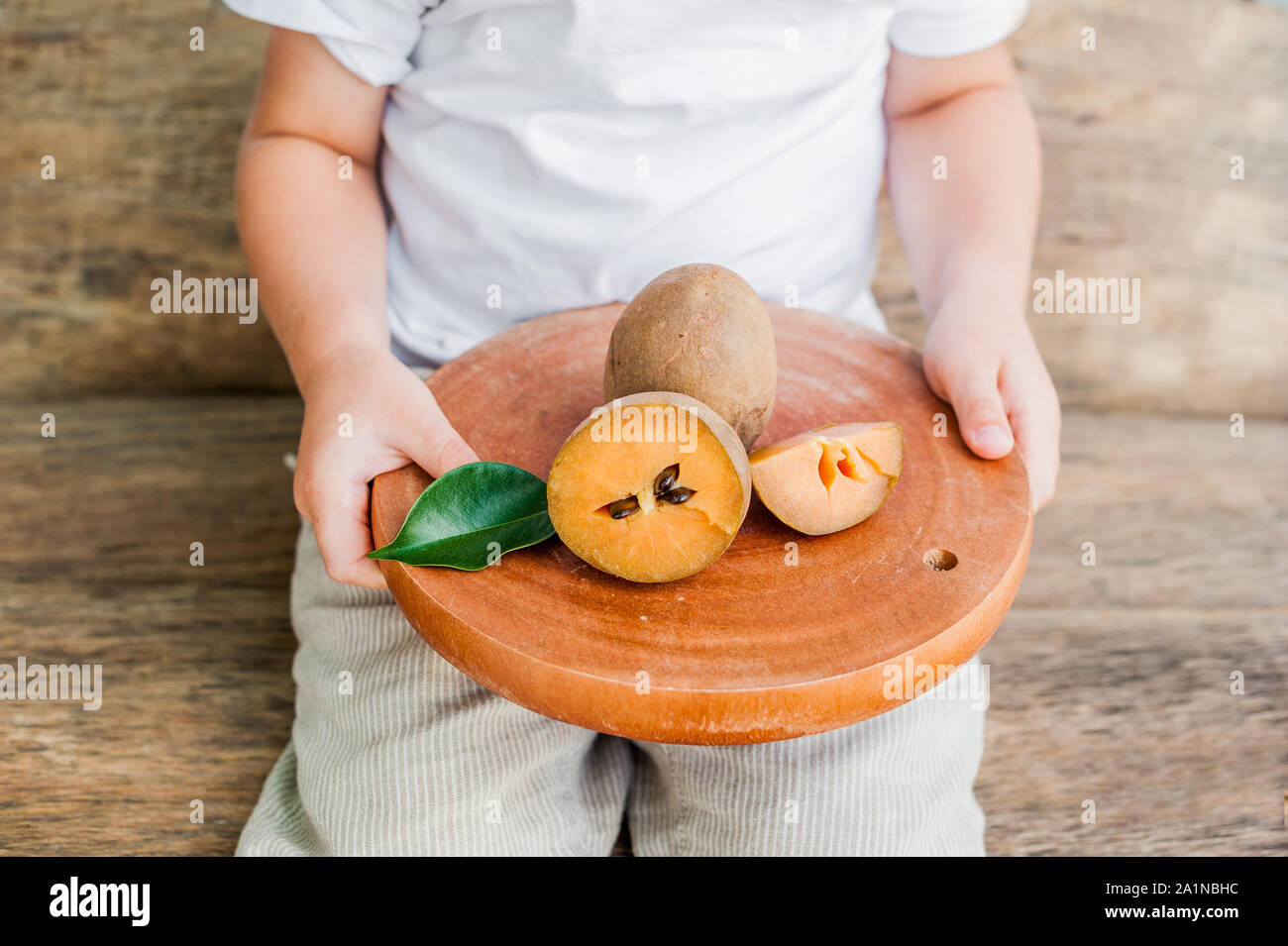 Hands holding a board with fresh sapodilla fruits on old wooden background Stock Photo
