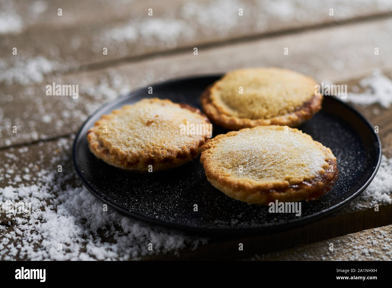 Three mince pies on a black plate on a rustic wooden table with snow Stock Photo