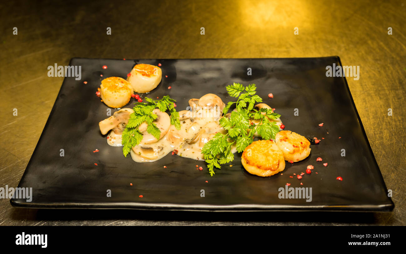 Scallops with mushroom sauce served on black plate Stock Photo