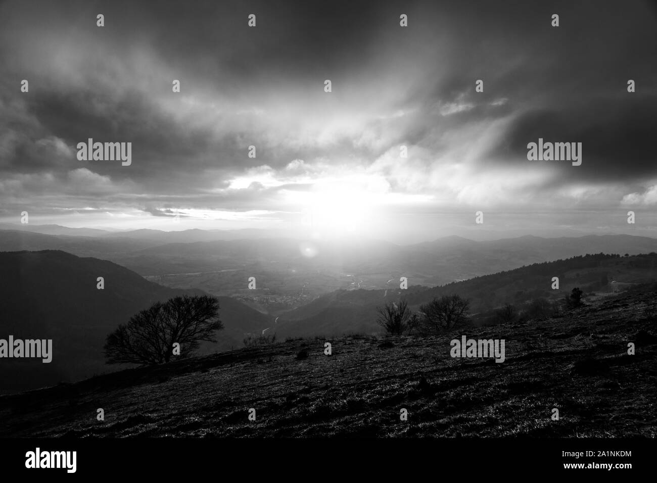 Moody sunset on Monte Cucco (Umbria, Italy), with tree in the foreground and sun filtering through clouds Stock Photo
