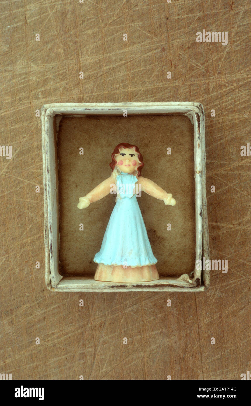 Small cardboard tray containing model of woman in full-length dress with blue puinafore standing with arms outstretched Stock Photo
