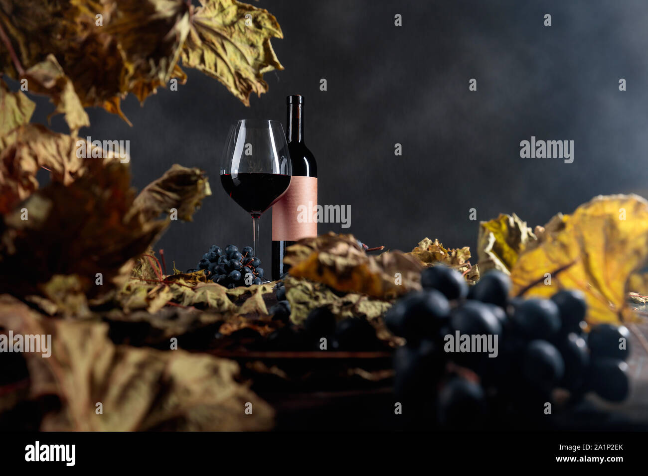 Bottle and glass of red wine on a table with dried vine leaves and blue ...