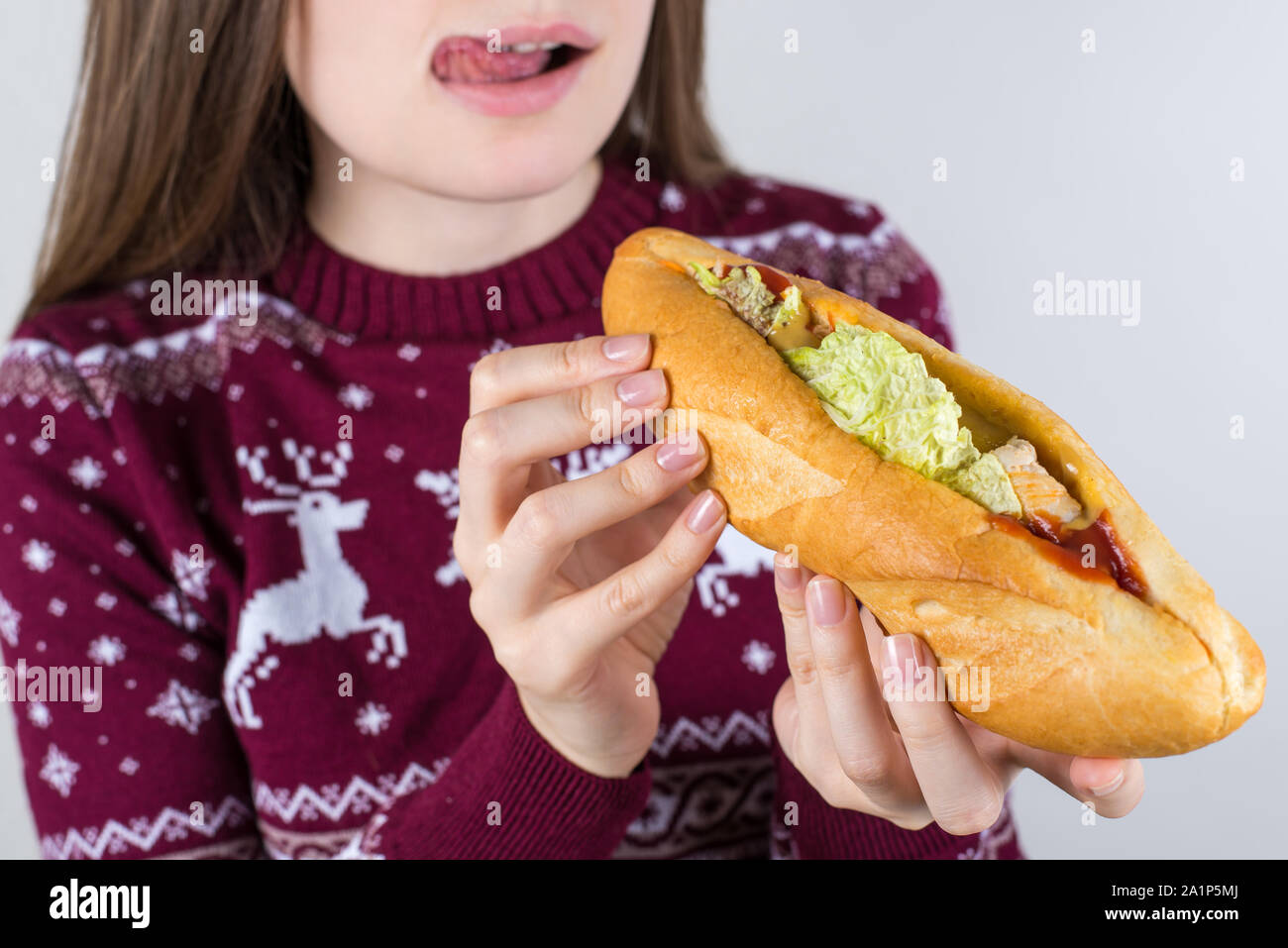 Cropped close up photo portrait of happy smiling satisfied tongue-out girl  holding long big burger in hands preparing for biting isolated grey color Stock Photo