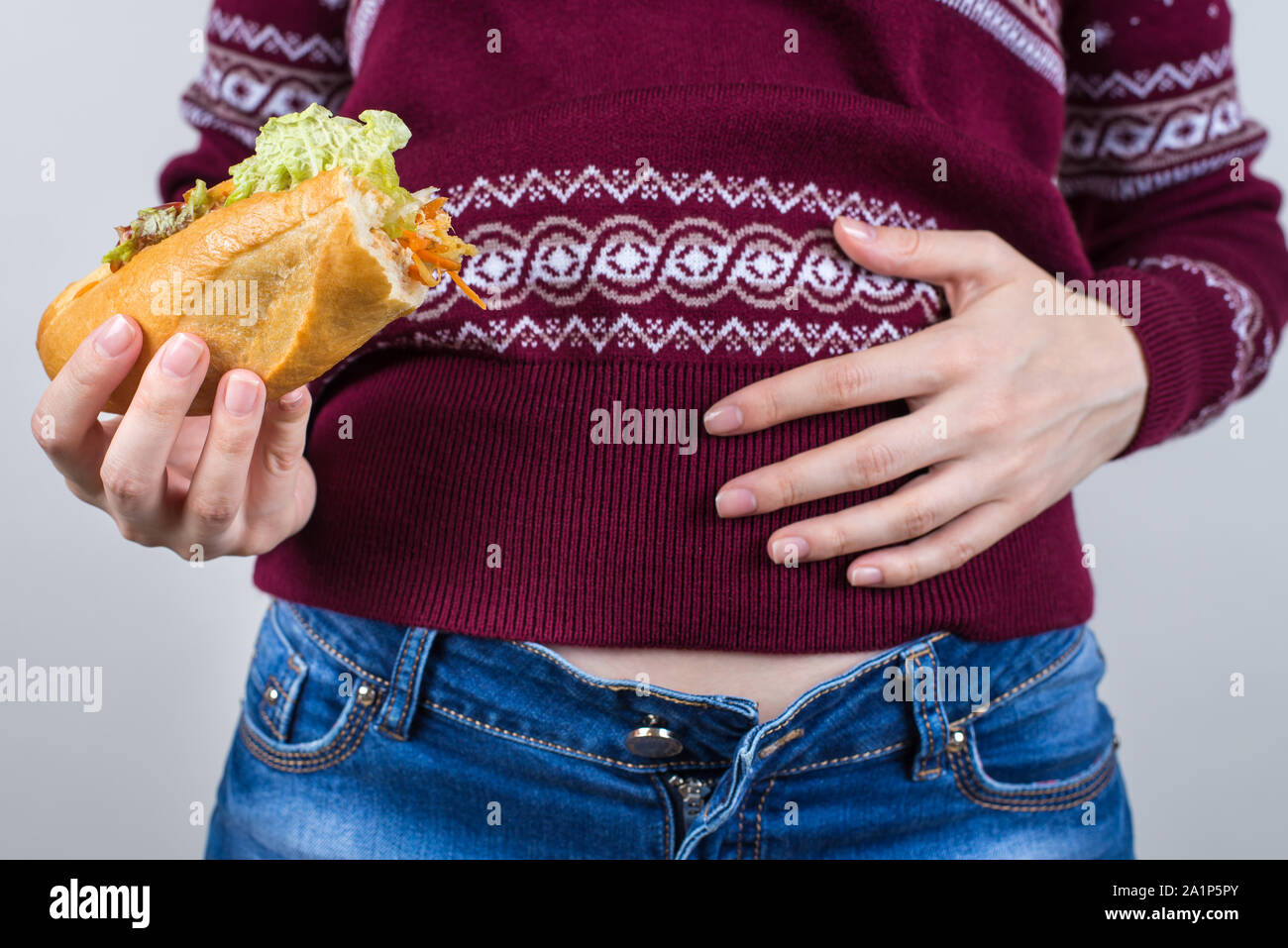 Over eating on holidays concept. Cropped close up photo of satisfied but feeling not perfect in abdomen girl holding large dish isolated grey backgrou Stock Photo