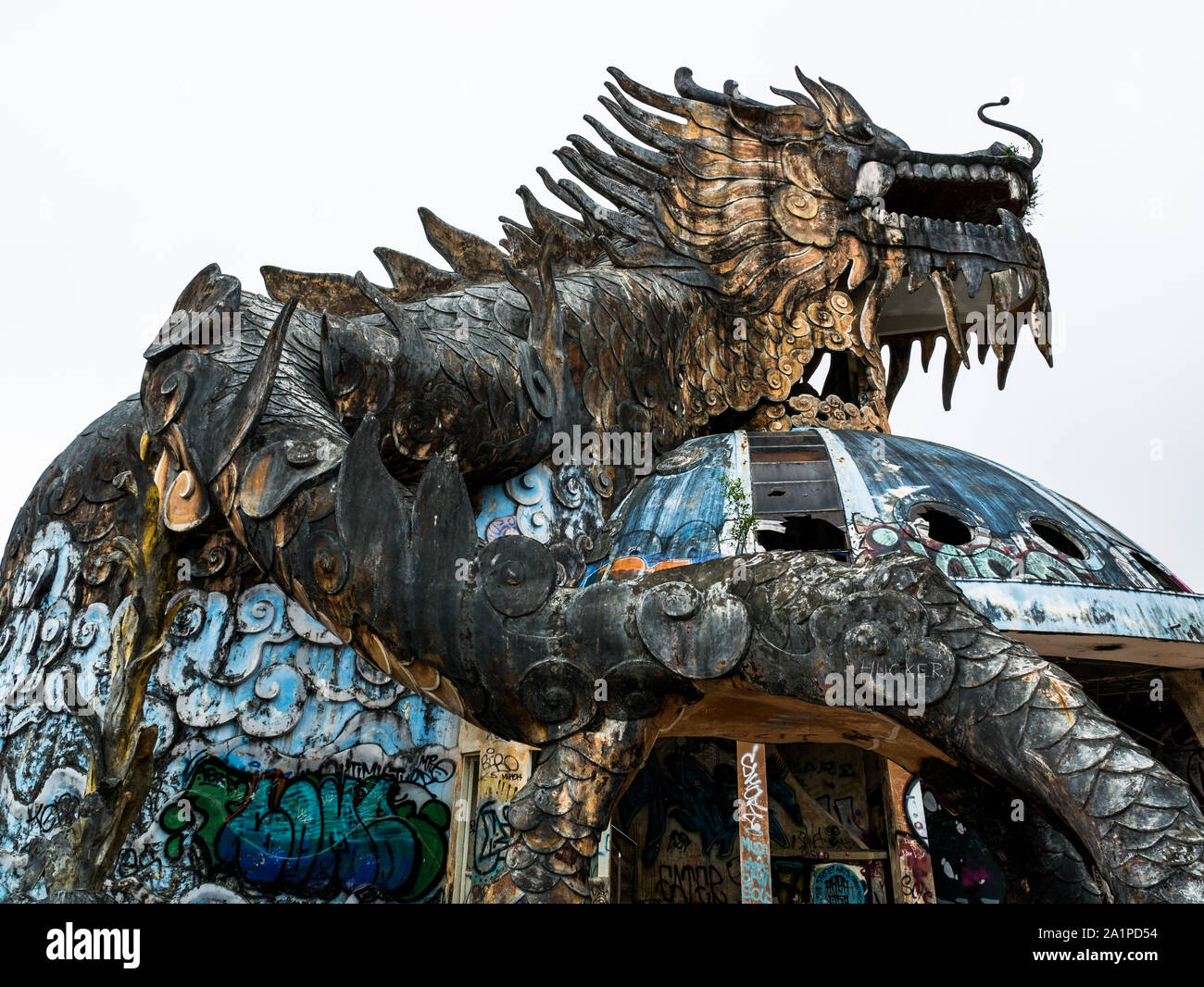 Huge and scary stone dragon with spikes and open mouth with teeth from below in wide angle at abandoned water park, Thuy Tien lake, Hue, Vietnam Stock Photo