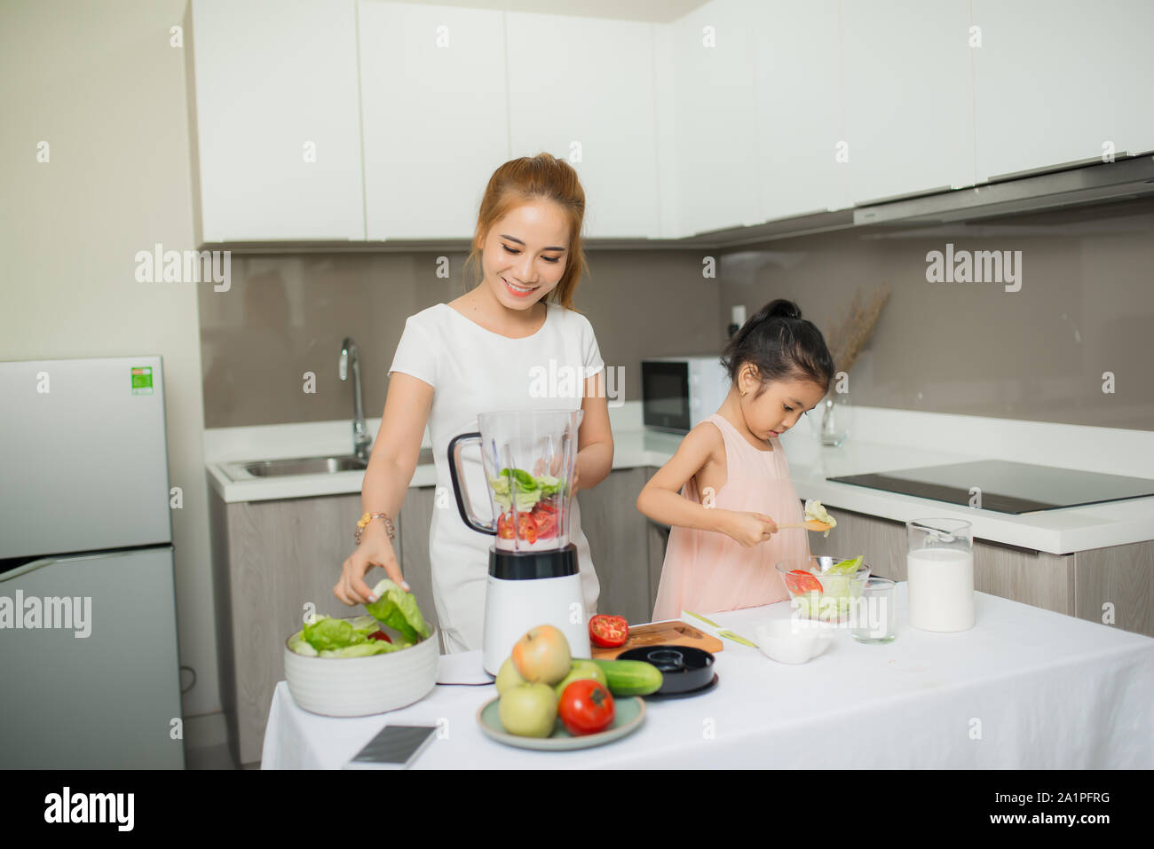 Young Asian mother and daughter making freshly squeezed tomato smoothies, daughter is very happy Stock Photo
