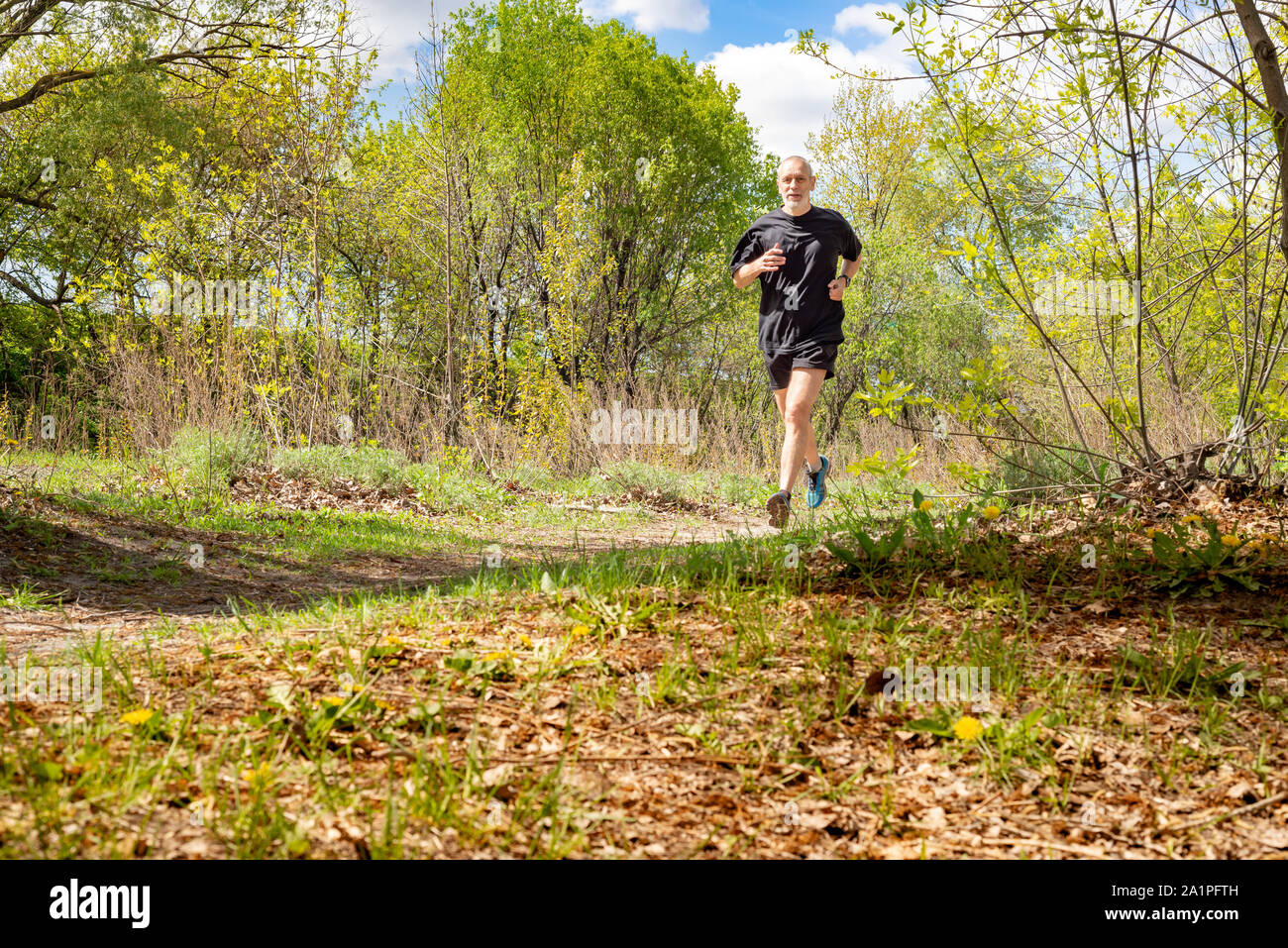 A senior man dressed in black  is running in the forest, during a warm autumn day Stock Photo
