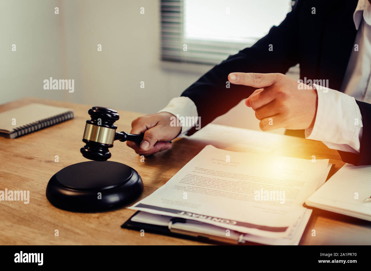 justice lawyer in black suit pointing finger and knocking wooden judge gavel with document on workplace desk in courtroom office Stock Photo