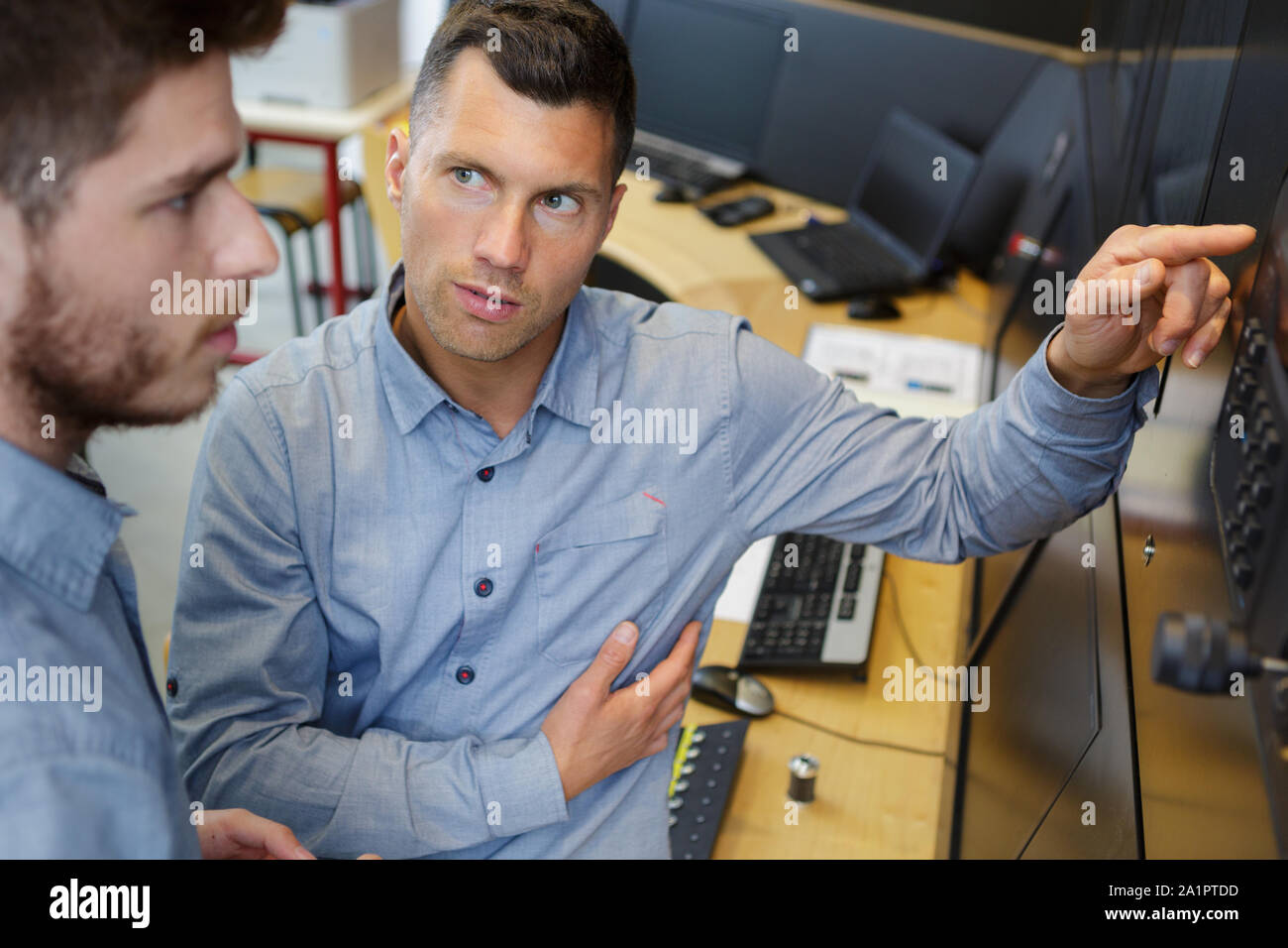 manager interrogating younger worker while pointing to computer monitor Stock Photo