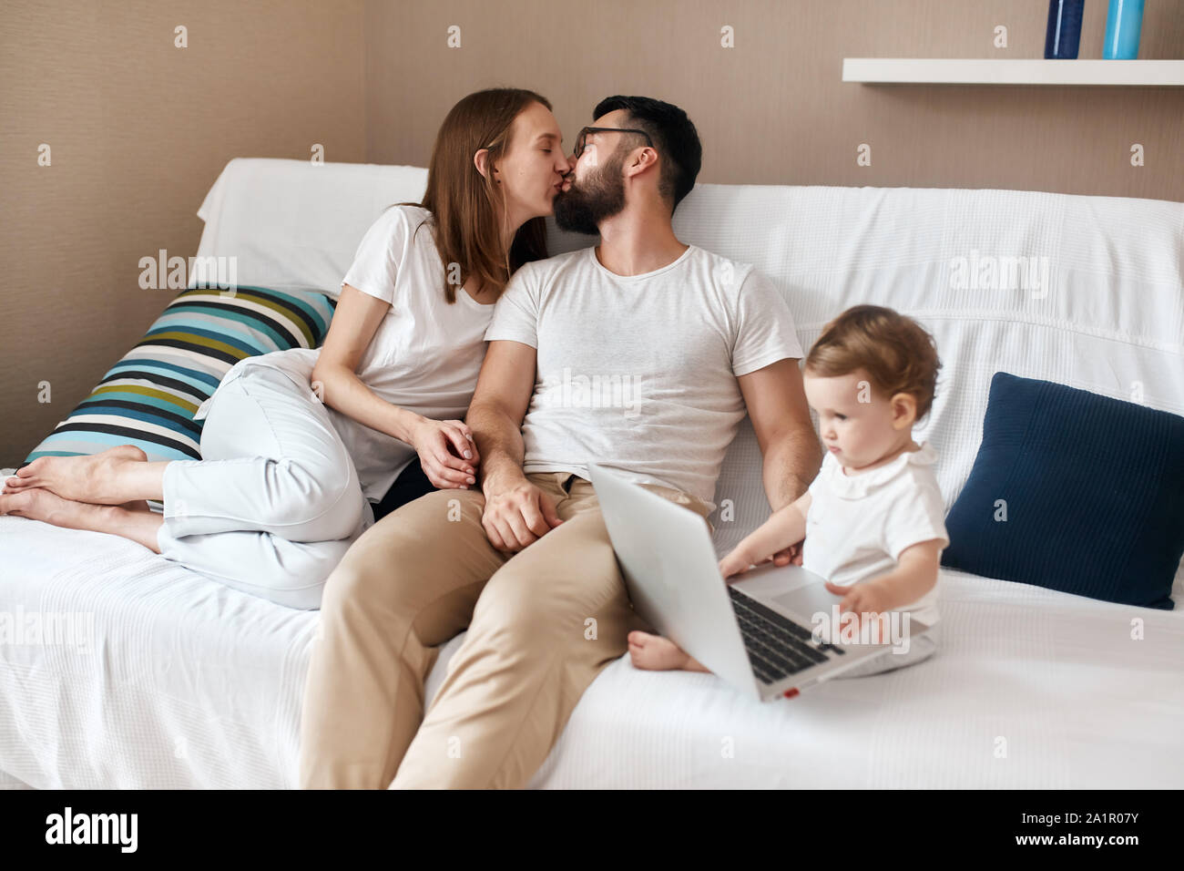 loving couple kissing while their baby watchcing cartoon on the laptop,  love, warm, tender feeling and emotion Stock Photo - Alamy