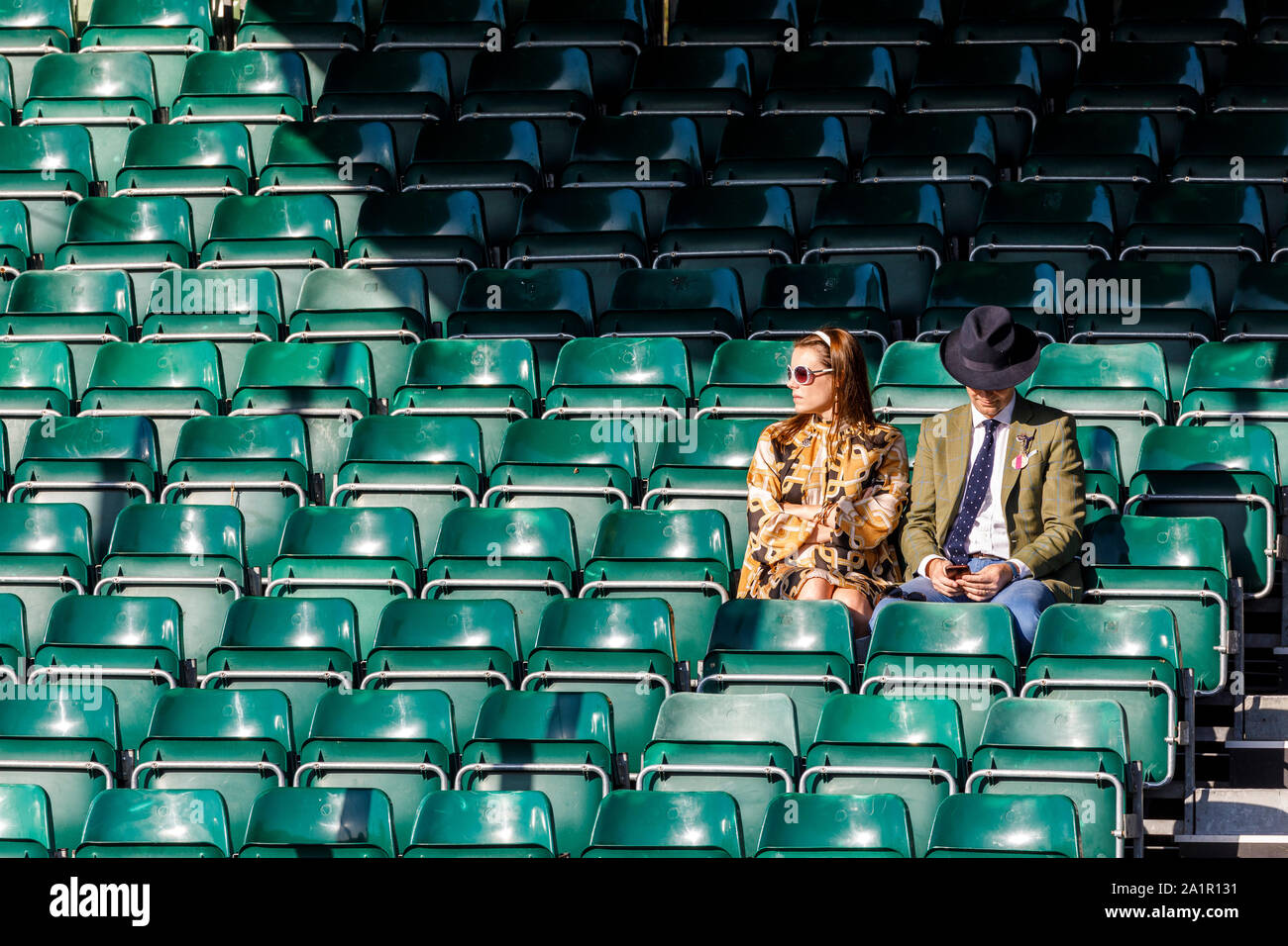 Well dressed couple waiting in an empty grandstand for track action in the sunlight at the 2019 Goodwood Revival, Sussex, UK. Stock Photo