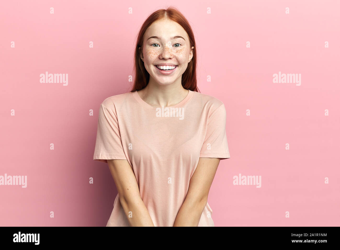 positive ginger girl keeps arms together, smiles gently, admires listening sweet voice of