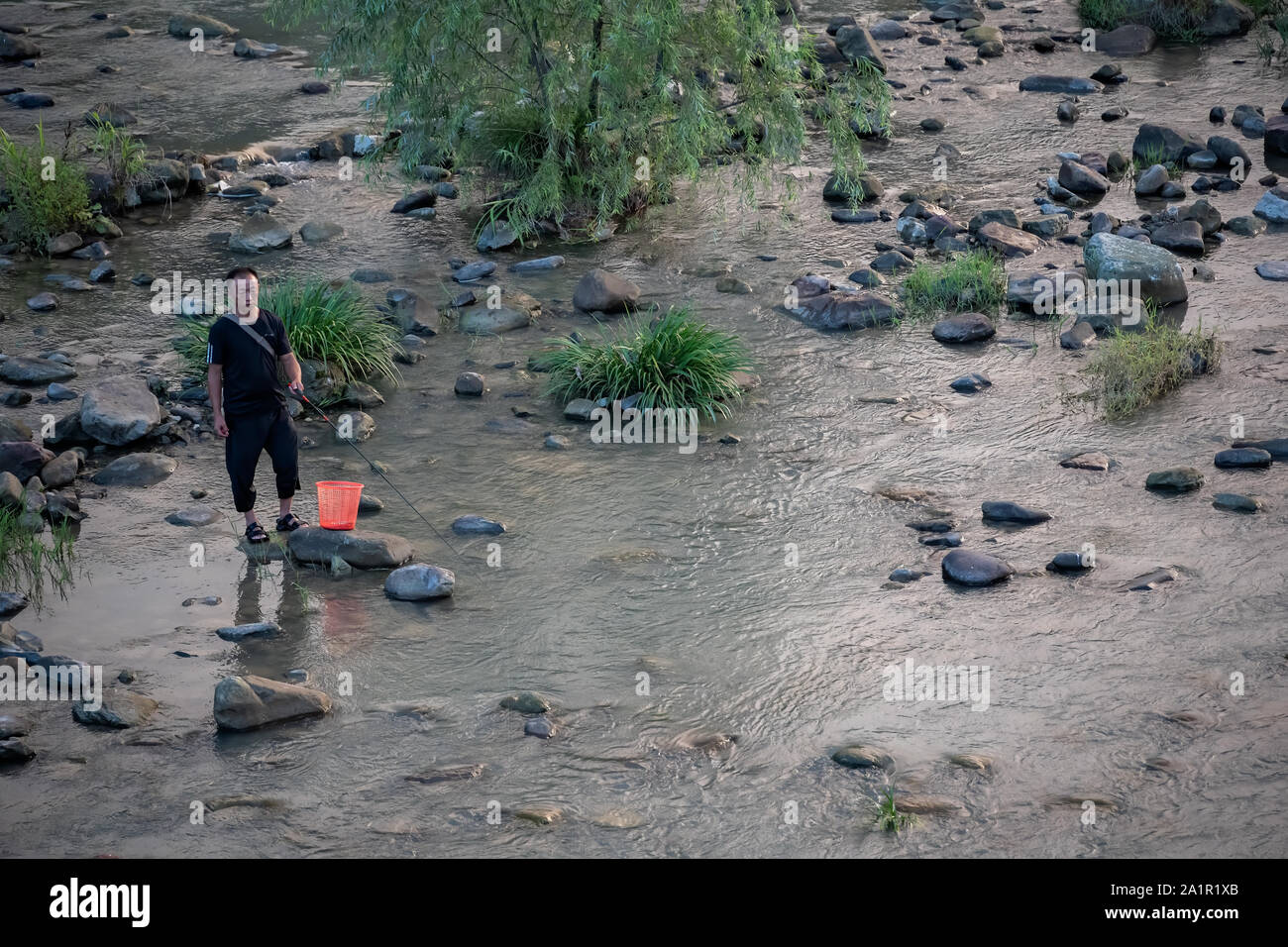 Wulingyuan, China -  August 2019 : Chinese fisherman standing in a shallow river Stock Photo
