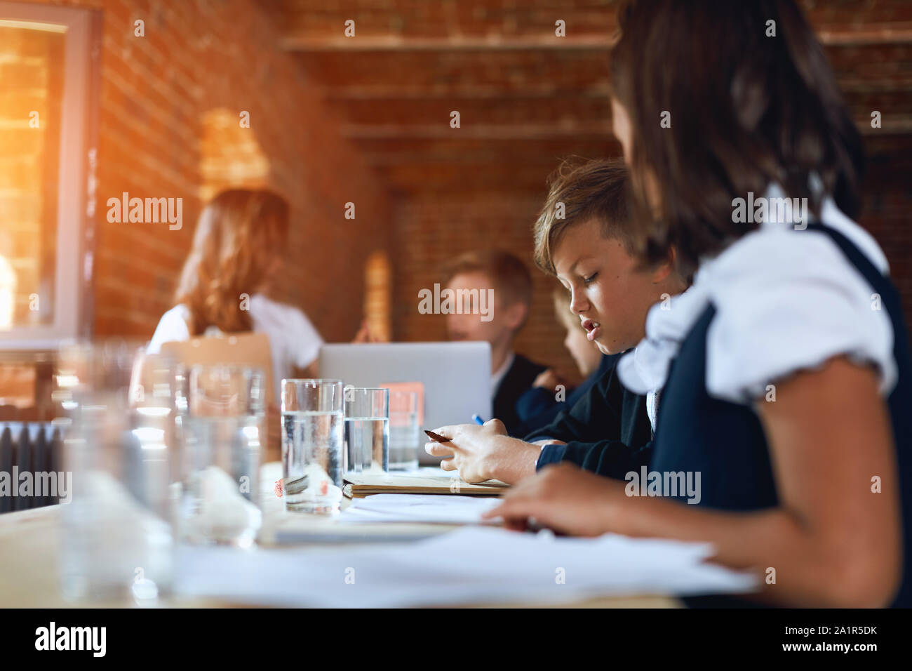 boy and girl in stylish office clothes taking aprt in the conference, eriting something on sheet of papre, close up side view photo Stock Photo