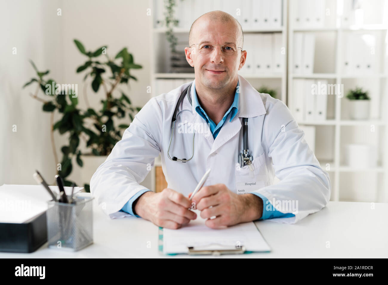 Young Successful Clinician In Eyeglasses And Whitecoat Sitting By