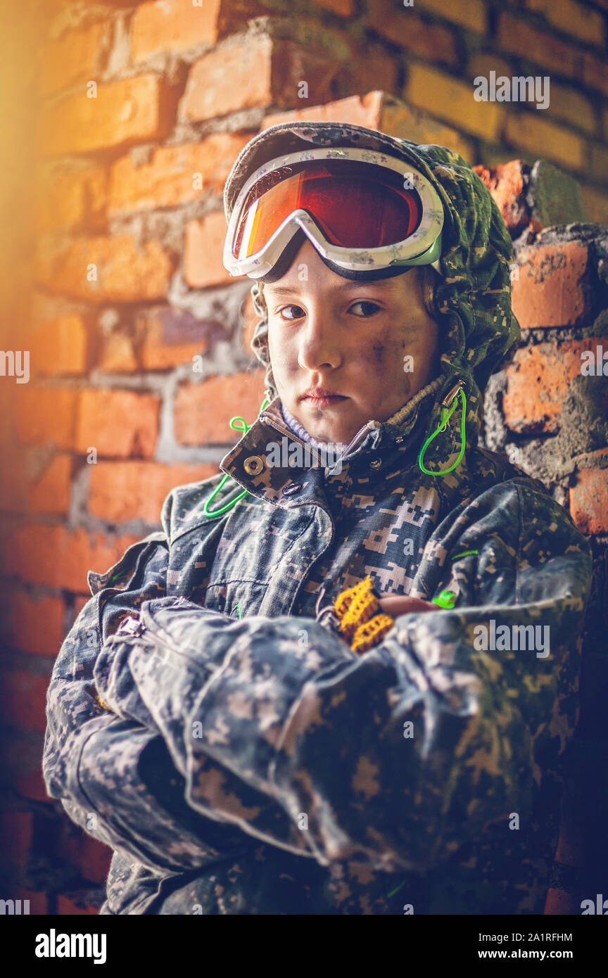Serious child in military uniform. Disappointed kid with crossing arms. Disillusioned young stalker in abandoned building. Girl with offended facial e Stock Photo