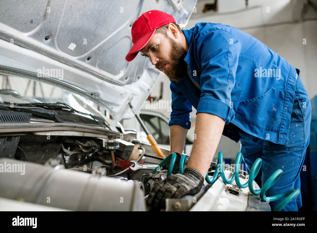 Bearded technician of car repair service with wrench examining engine