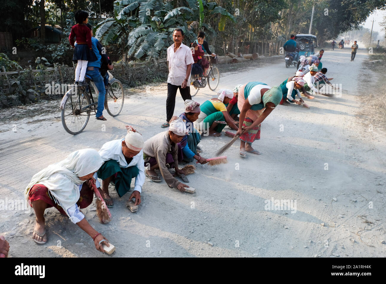 Women clean a road of sand and dust in Tangla, Assam, India Stock Photo