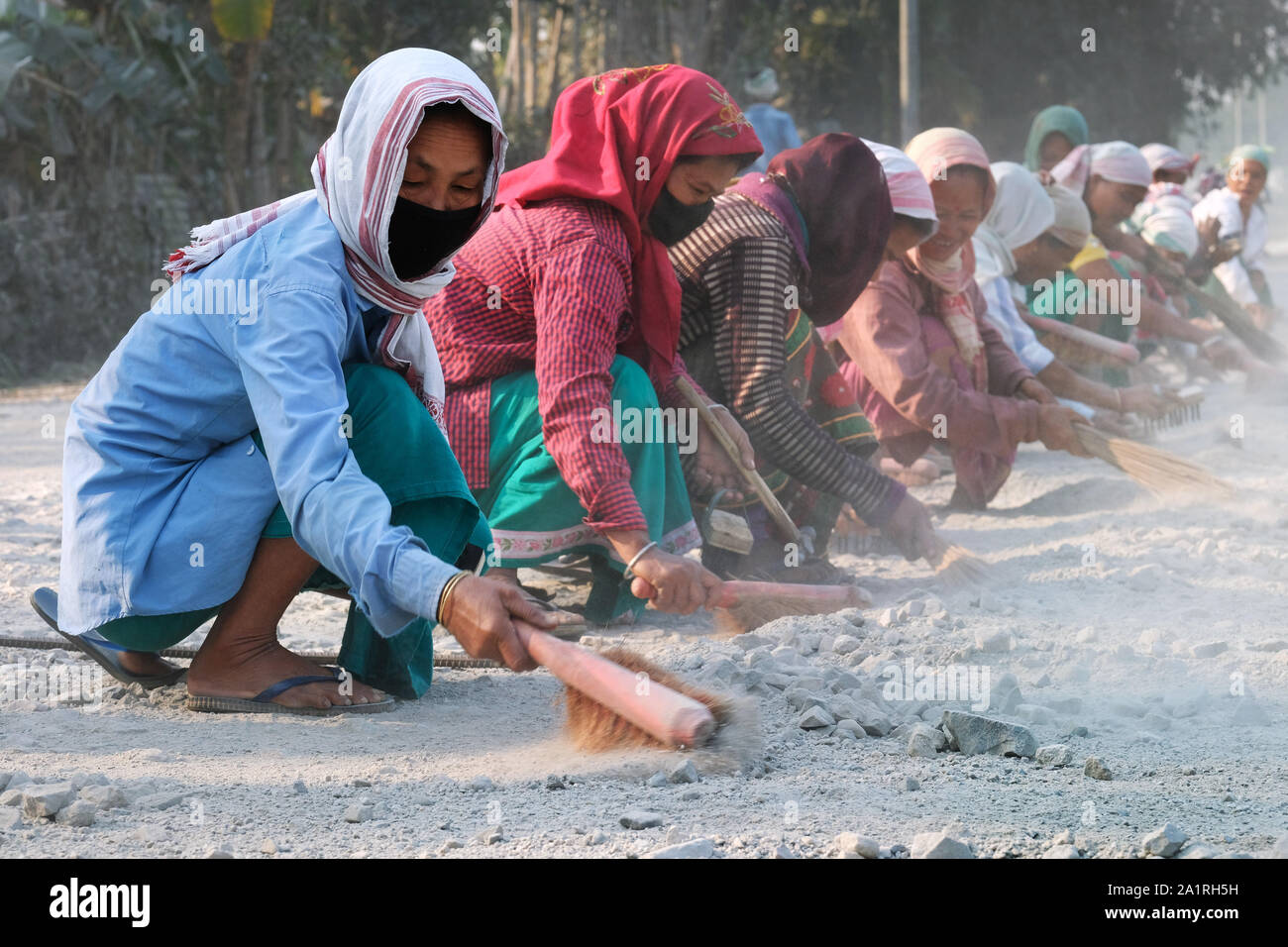 Women clean a road of sand and dust in Tangla, Assam, India Stock Photo