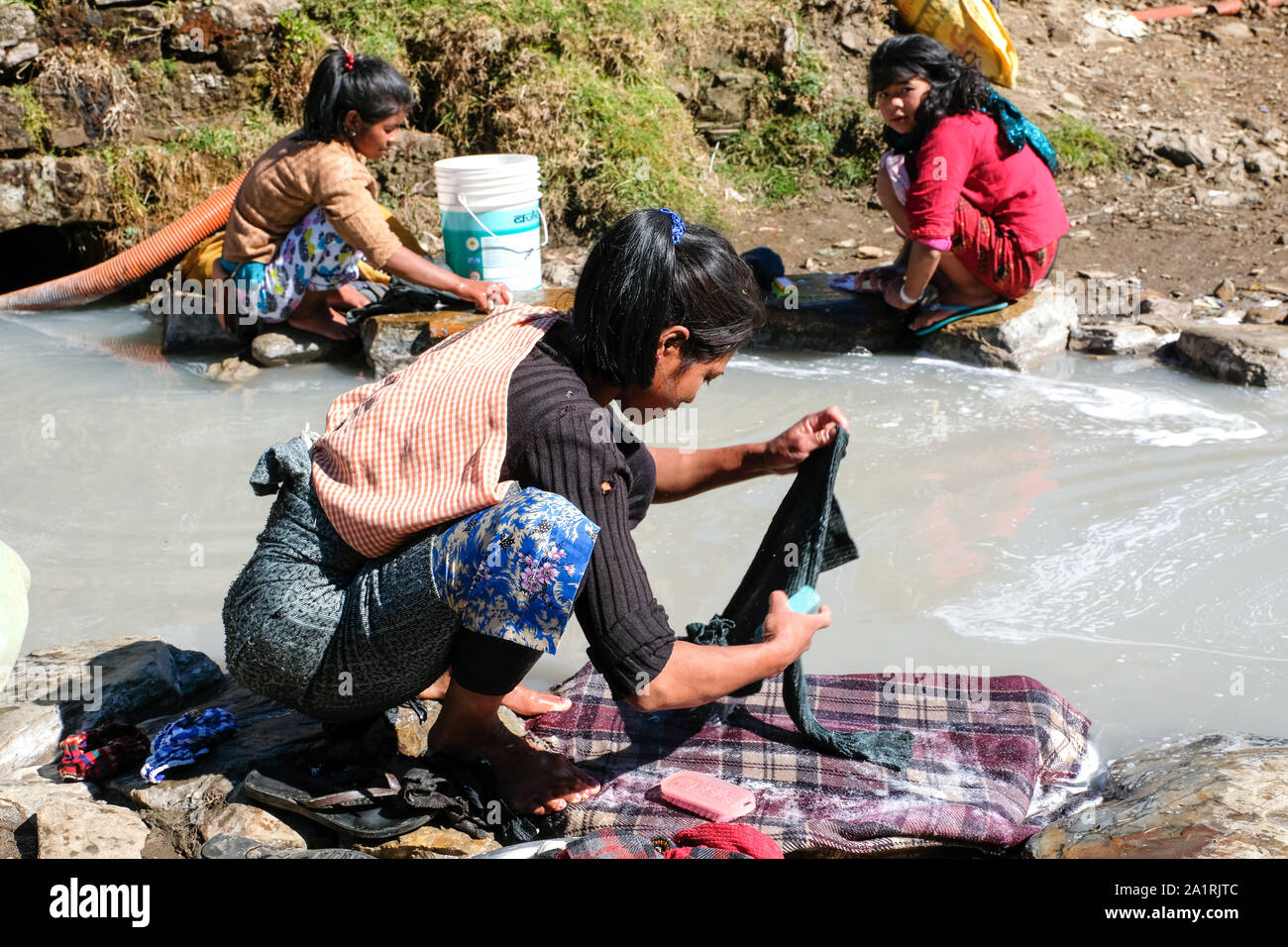 Women and girls wash clothes in a dirty stream. State of Meghalaya