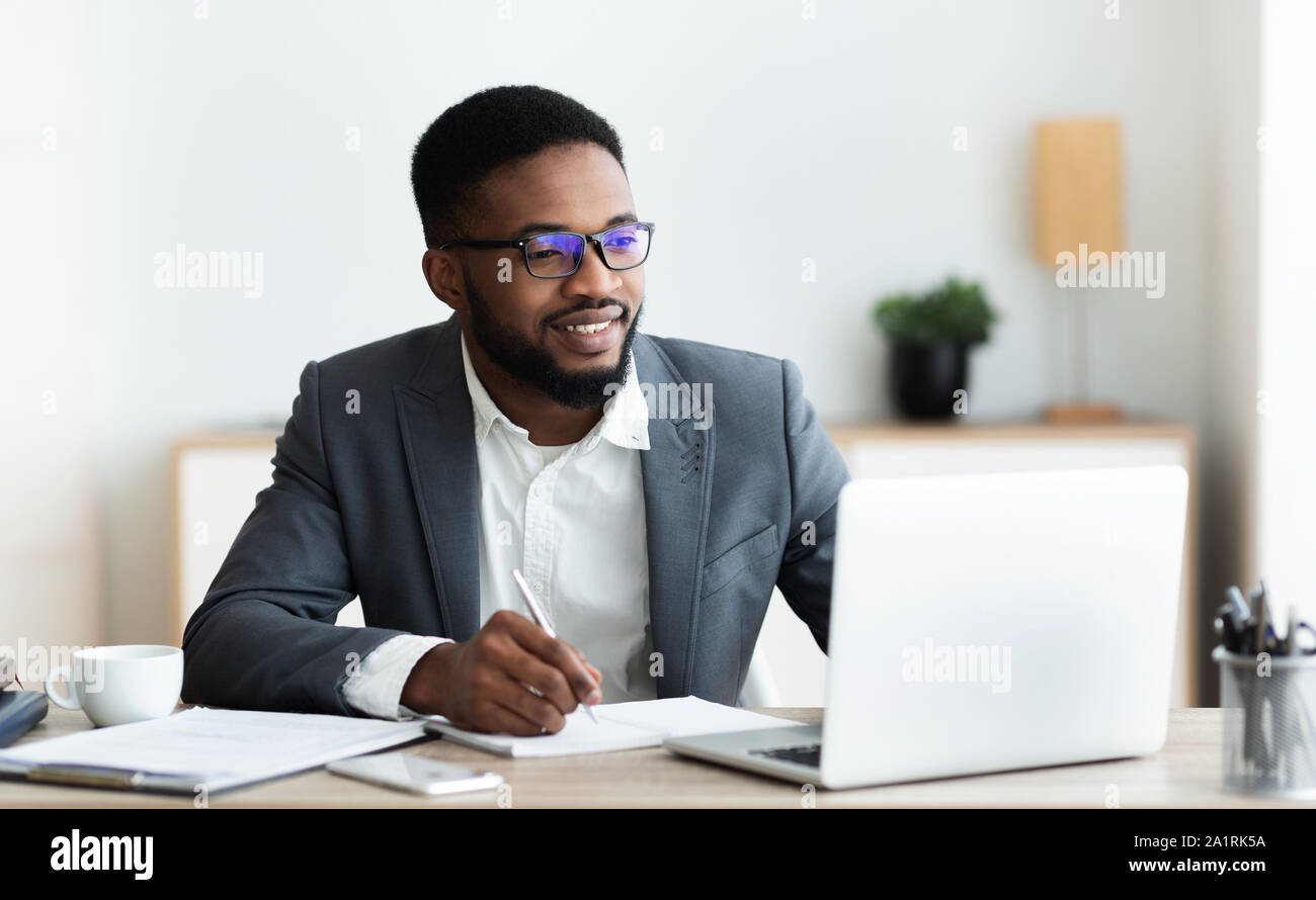 Handsome black entrepreneur working on laptop and taking notes Stock Photo