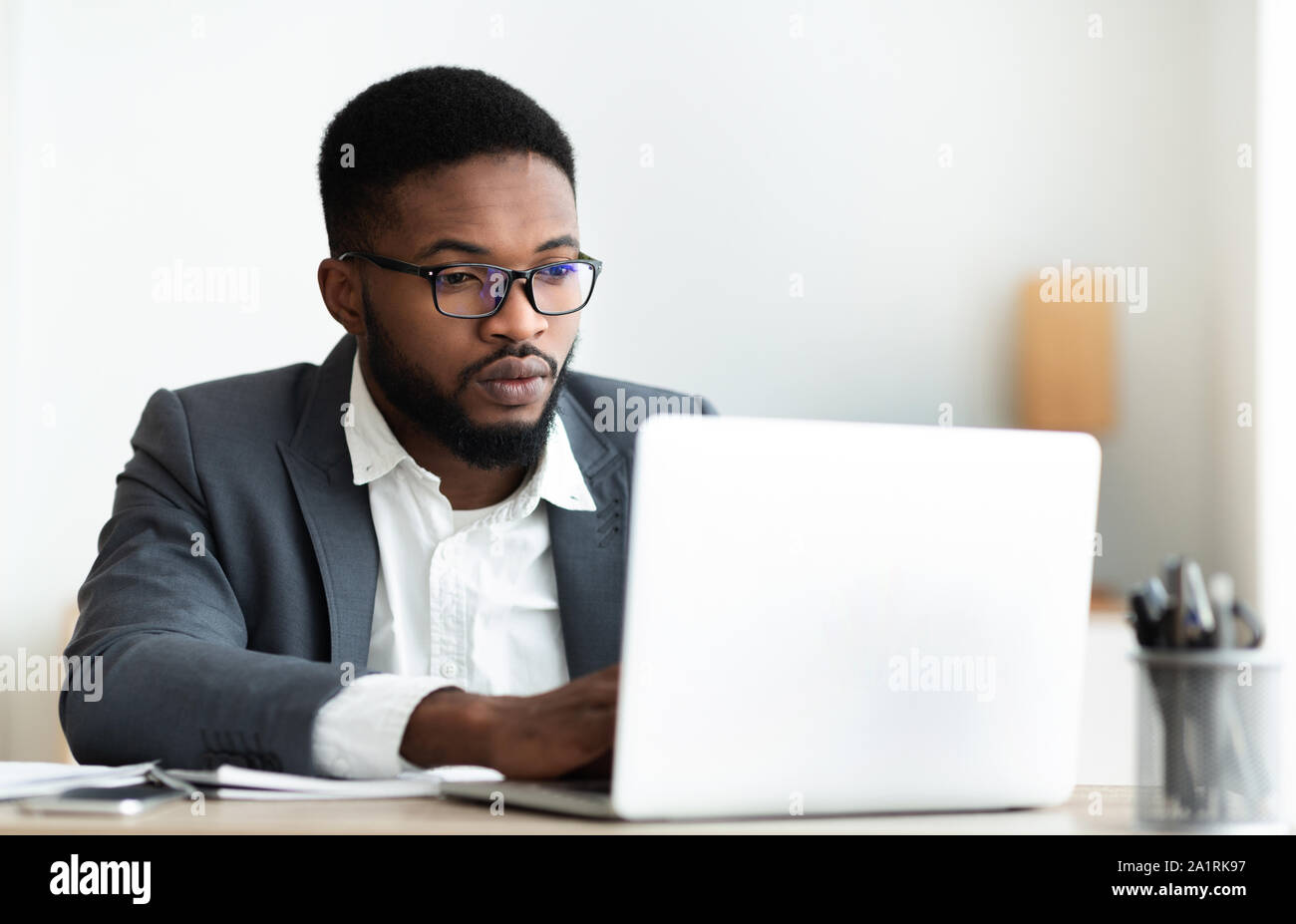 Serious black businessman working on laptop in office Stock Photo
